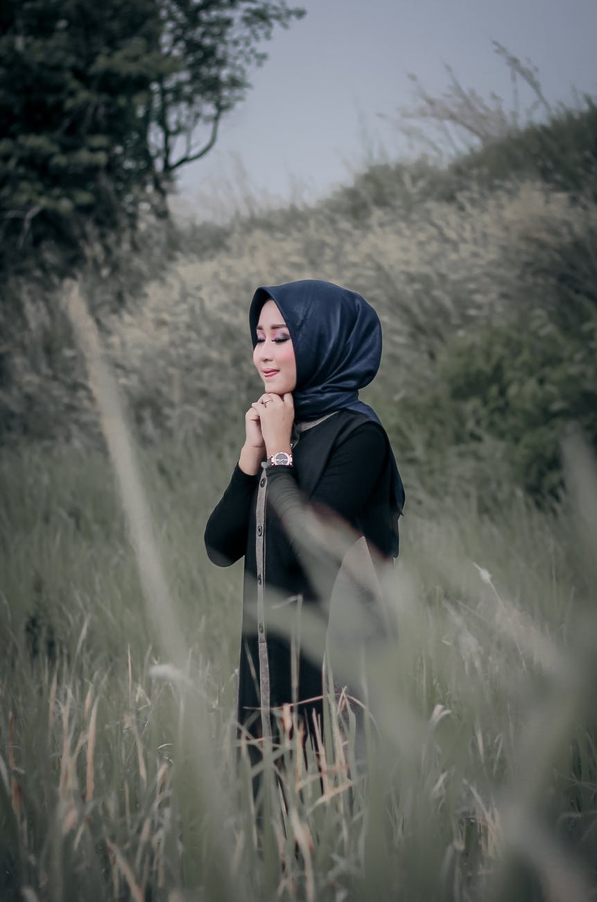photo of smiling woman in black hijab standing in grass field with her eyes closed